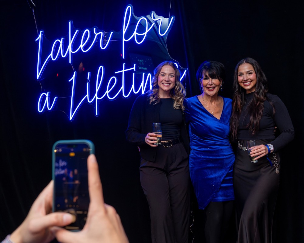 Two girls dressed in black and President Mantella stand in front of Laker for a Lifetime neon sign
